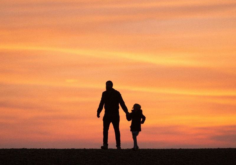 A father and young child walking hand in hand at sunset
