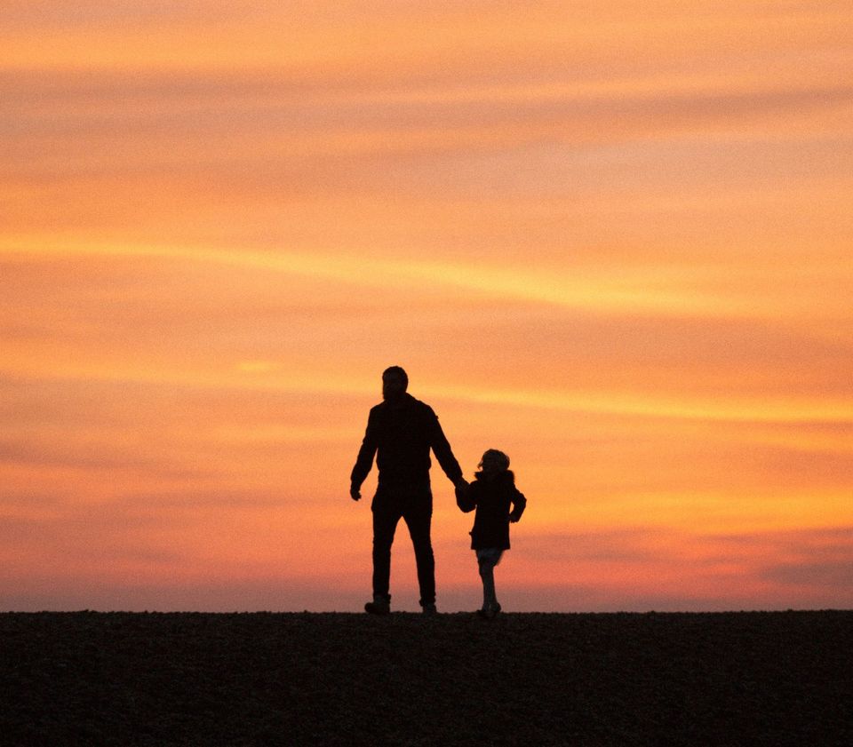 A father and young child walking hand in hand at sunset