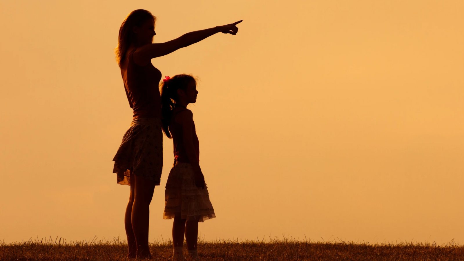 A mother and her young daughter at sunset, looking out towards the horizon